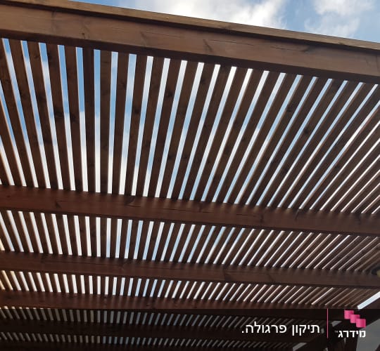 פרגולה מעץ עם קורות אופקיות בשמיים בהירים